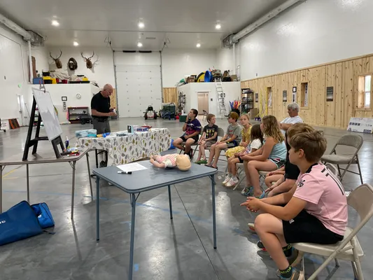 Instructor teaching seated youth with an infant CPR manikin on the table