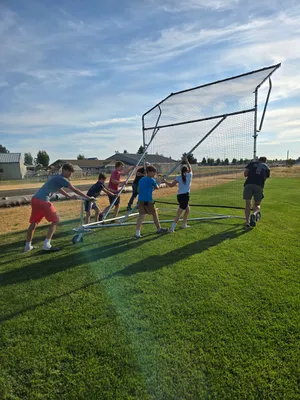 Group of youth and adults rolling the backstop across the grass field