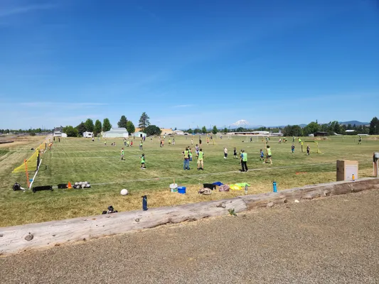 Campers spread across the grass field for soccer drills with a mountain in the distance