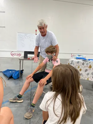Instructor demonstrating an arm sling beside a whiteboard reading Check, Call, Care