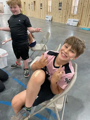 Youth grinning and holding up peace signs after practicing bandaging