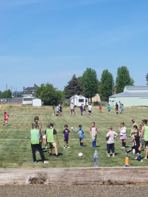 Campers in colored pinnies practicing soccer drills on the grass field