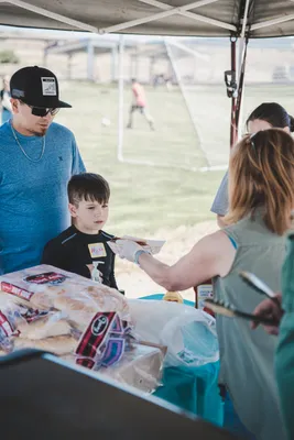 A volunteer giving a hotdog to a boy.