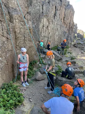 Youth in climbing helmets with ropes at the base of a basalt cliff
