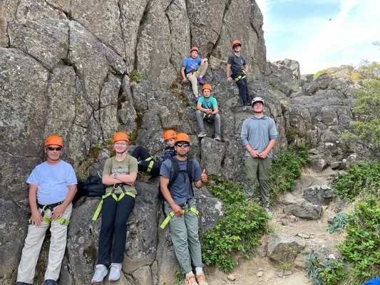 Group of youth and leaders in climbing helmets posing on a basalt rock outcrop
