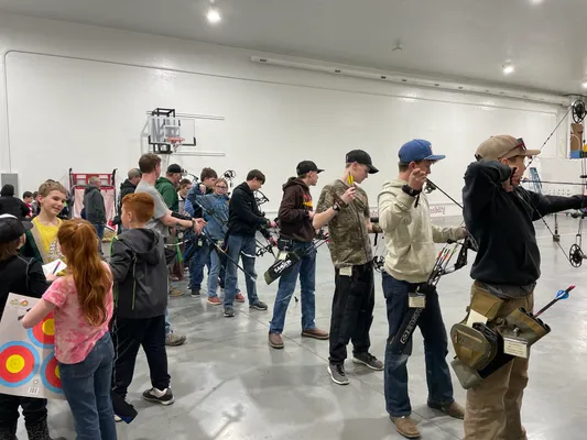 Youth with compound bows on the shooting line with targets visible