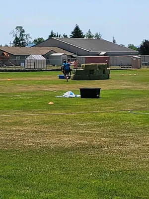 Youth playing with a small pool behind a fort made of hay bales.